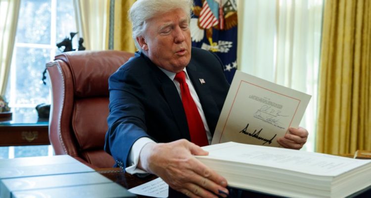 President Donald Trump grabs a box containing the tax bill after signing it in the Oval Office of the White House, Friday, Dec. 22, 2017, in Washington. (AP Photo/Evan Vucci)