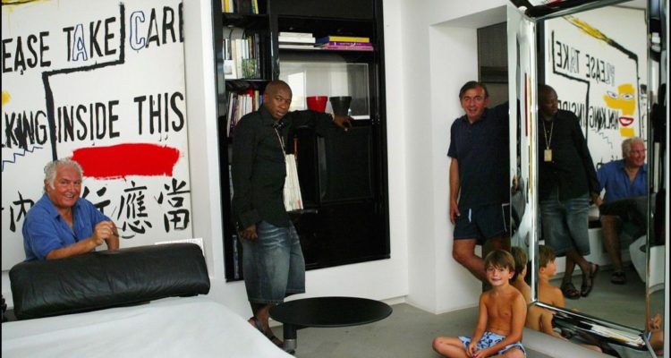 FRANCE - JULY 01: From left to right : Tony Shafrazi, Mohamed Dia, Enrico Navarra, and Enrico's son Doriano - At Enrico Navarra's villa, posing in front of a piece of art by Andy Warhol and Jean Michel Basquiat - Dia wears a costume by Smalto : he is the ambassador of the Smalto fashion house in the US in Le Muy, France in July, 2003. (Photo by Eric TRAVERS/Gamma-Rapho via Getty Images)