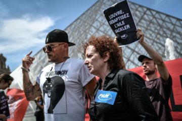 Nancy Goldin (C), photographer and founder of P.A.I.N. (Prescription Addiction Intervention Now) association - created to respond to the opioid crisis - and Fred Bladou (L), mission head of French NGO Aides, take part in a protest on July 1, 2019 in front of the Louvre museum in Paris, to condemn the museum's ties with the Sackler family, billionaire donors accused of pushing to sell a highly addictive painkiller blamed for tens of thousands of deaths. - The Sacklers have been high-profile philanthropists to cultural institutions such as the Tate in London and the Guggenheim in New York, but museums and galleries have recently been rebuffing their donations because of the opioid crisis fallout. The most recent museum to cut ties with the Sackler family is New York's Metropolitan Museum, which announced earlier this month that it will cease accepting gifts from the family. (Photo by STEPHANE DE SAKUTIN / AFP)        (Photo credit should read STEPHANE DE SAKUTIN/AFP/Getty Images)
