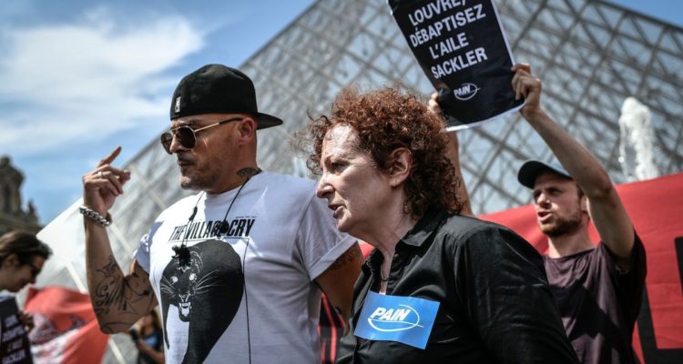 Nancy Goldin (C), photographer and founder of P.A.I.N. (Prescription Addiction Intervention Now) association - created to respond to the opioid crisis - and Fred Bladou (L), mission head of French NGO Aides, take part in a protest on July 1, 2019 in front of the Louvre museum in Paris, to condemn the museum's ties with the Sackler family, billionaire donors accused of pushing to sell a highly addictive painkiller blamed for tens of thousands of deaths. - The Sacklers have been high-profile philanthropists to cultural institutions such as the Tate in London and the Guggenheim in New York, but museums and galleries have recently been rebuffing their donations because of the opioid crisis fallout. The most recent museum to cut ties with the Sackler family is New York's Metropolitan Museum, which announced earlier this month that it will cease accepting gifts from the family. (Photo by STEPHANE DE SAKUTIN / AFP) (Photo credit should read STEPHANE DE SAKUTIN/AFP/Getty Images)