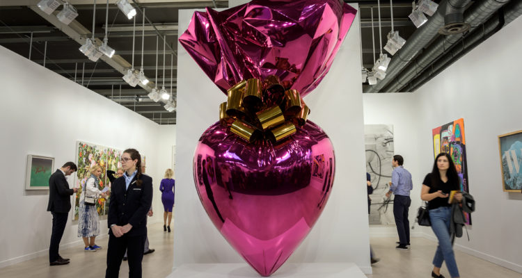 Visitors stand next to an artwork by Jeff Koons entitled "Sacred Heart (Magenta/Gold)" at the Gagosian gallery exhibition space during a preview day of Art Basel, the world's premier modern and contemporary art fair, on June 12, 2019 in Basel. - Thousand of art collectors, art dealers, artists, curators and art lovers are expected to attend the annual meeting place of the art community with 290 of the world's leading galleries showing the works of over 4,000 artists. (Photo by FABRICE COFFRINI / AFP) (Photo credit should read FABRICE COFFRINI/AFP/Getty Images)